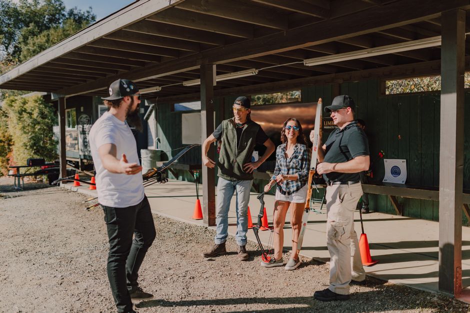 Four people engaged in a home relocation process outside a building with a large covered area, where a removal van is parked nearby. The individual on the left, wearing a white t-shirt and a cap, appe